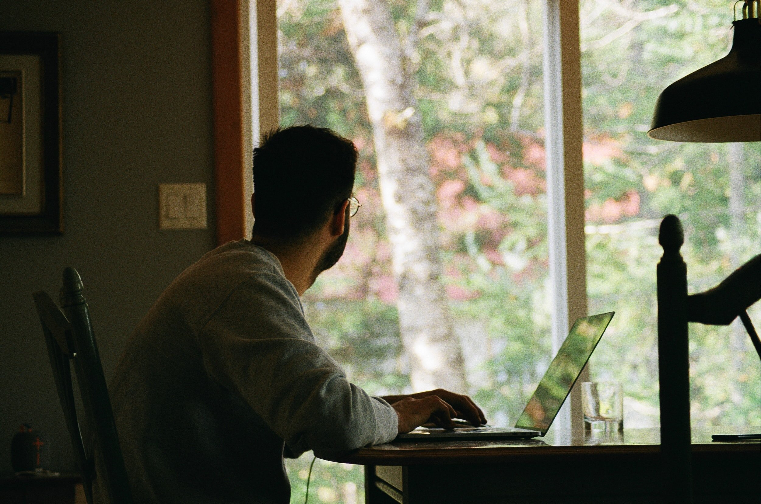 Man working at a laptop from a table looking out a sliding glass door